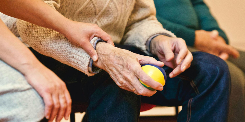 Younger hand holding hand of older person that is holding a yellow ball