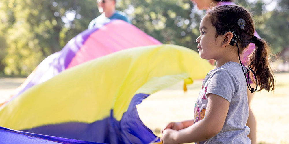 A child with a cochlear implant holding a parachute.